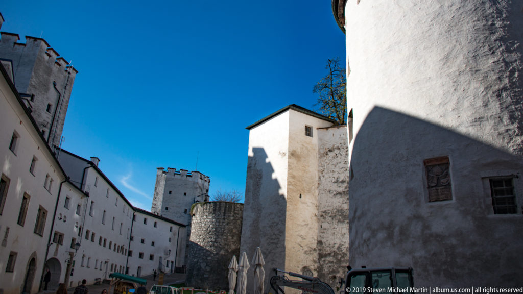 Whitewashed fortress walls and towers enclosing a sunlit interior passage beneath a deep blue sky.