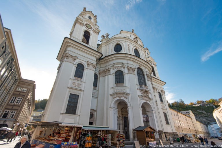 Oblique view of the white Kollegienkirche with one tower prominent above market stalls in Universitätsplatz.