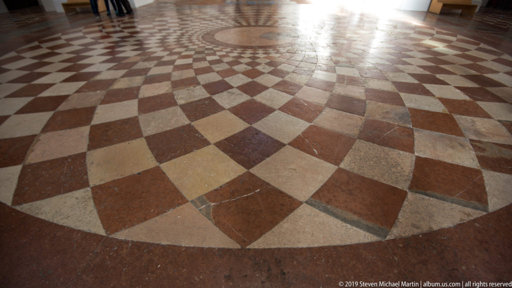 Close view of red, cream, and gray stone floor laid in concentric geometric bands inside the Kollegienkirche.