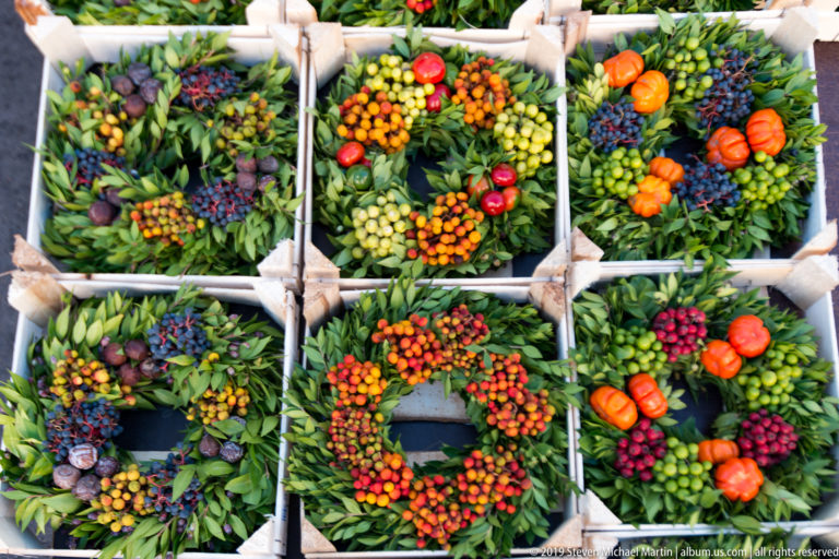 Overhead view of green foliage wreaths decorated with red, orange, yellow, and dark berries in market crates.
