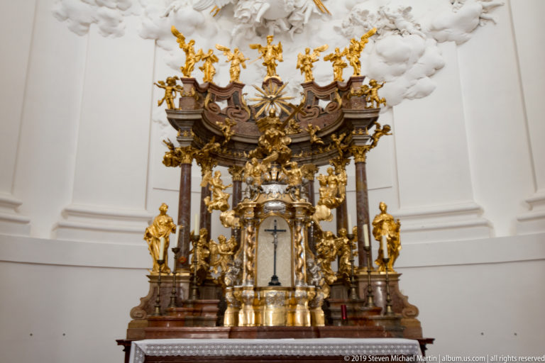 Highly gilded Baroque altar or shrine with dark columns, sculpted figures, and a small central glazed niche.