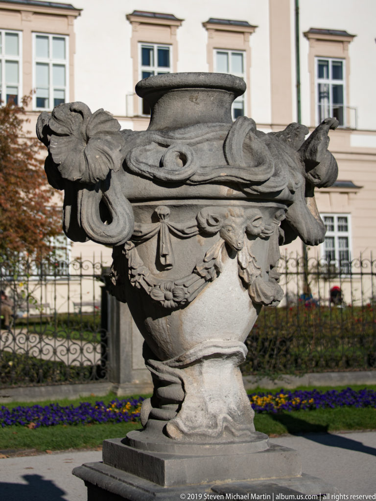 Large carved stone garden urn with scrolling handles, garlands, floral ornament, and pedestal before Mirabell Palace.