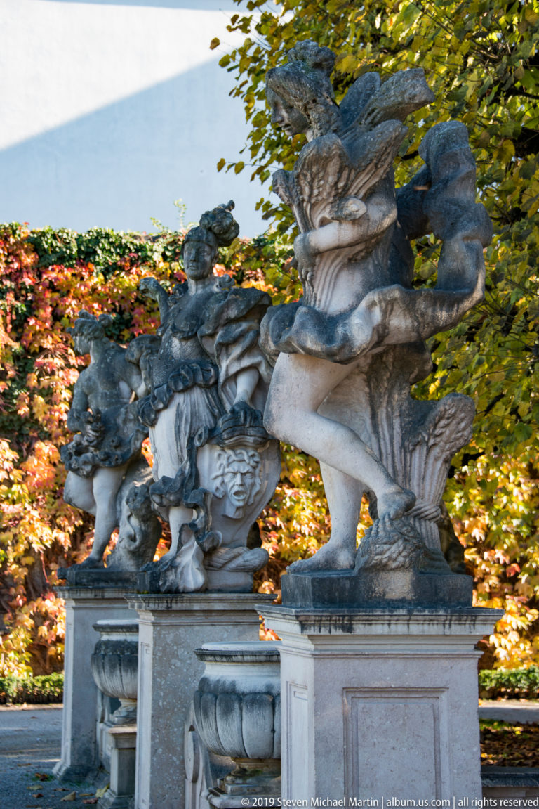 Baroque stone sculpture group of twisting human figures on a pedestal, framed by autumn foliage in Mirabell Gardens.