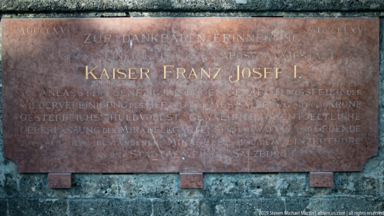 Reddish stone memorial plaque with gilded German inscription KAISER FRANZ JOSEF I set into a darker wall.