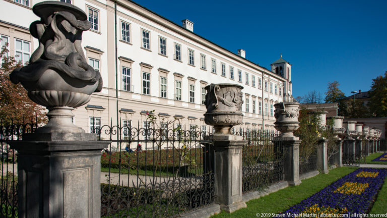 Ornamental iron garden fence with carved stone urns and floral finials in front of the long Mirabell Palace façade.