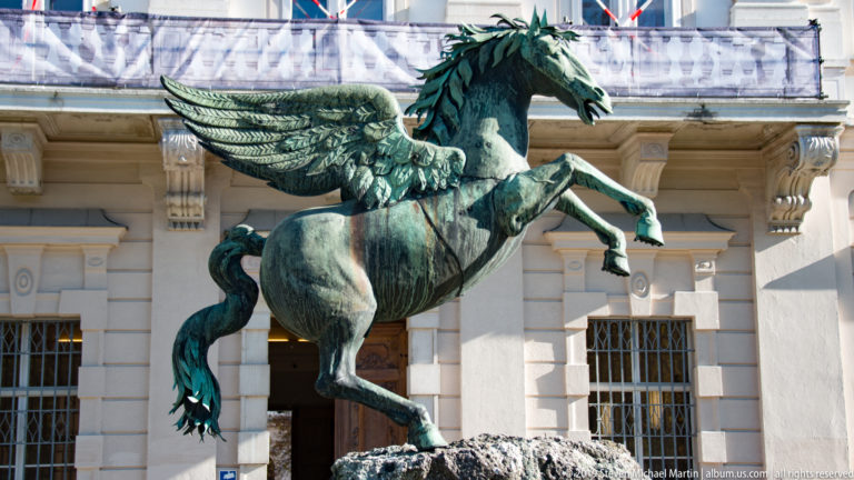 Green-patinated Pegasus sculpture with spread wings and raised forelegs in front of the pale façade of Mirabell Palace.