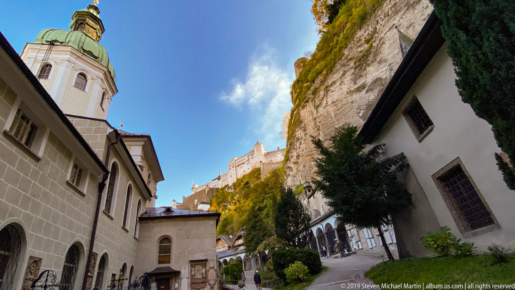 Upward view between St. Peter’s Abbey buildings and the Mönchsberg cliff, with Hohensalzburg Fortress rising above the precinct.