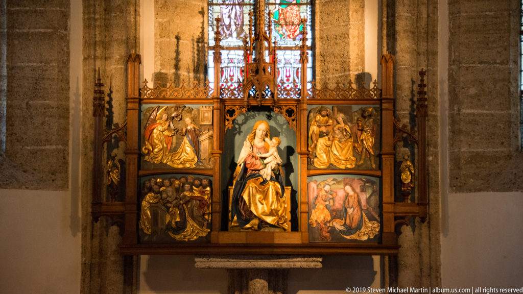 Polychrome winged altarpiece with the Virgin and Child at center, carved relief panels, gilding, and stained glass above.