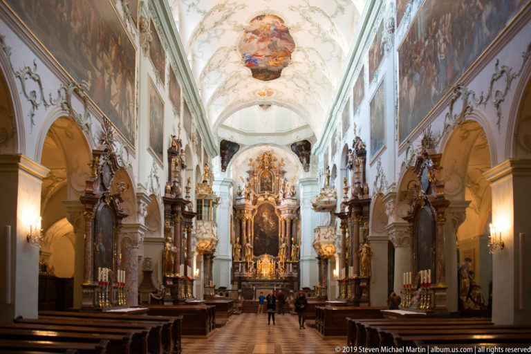 Central aisle of St. Peter's Abbey Church leading toward the ornate high altar, with side altars and vaulted ceiling.