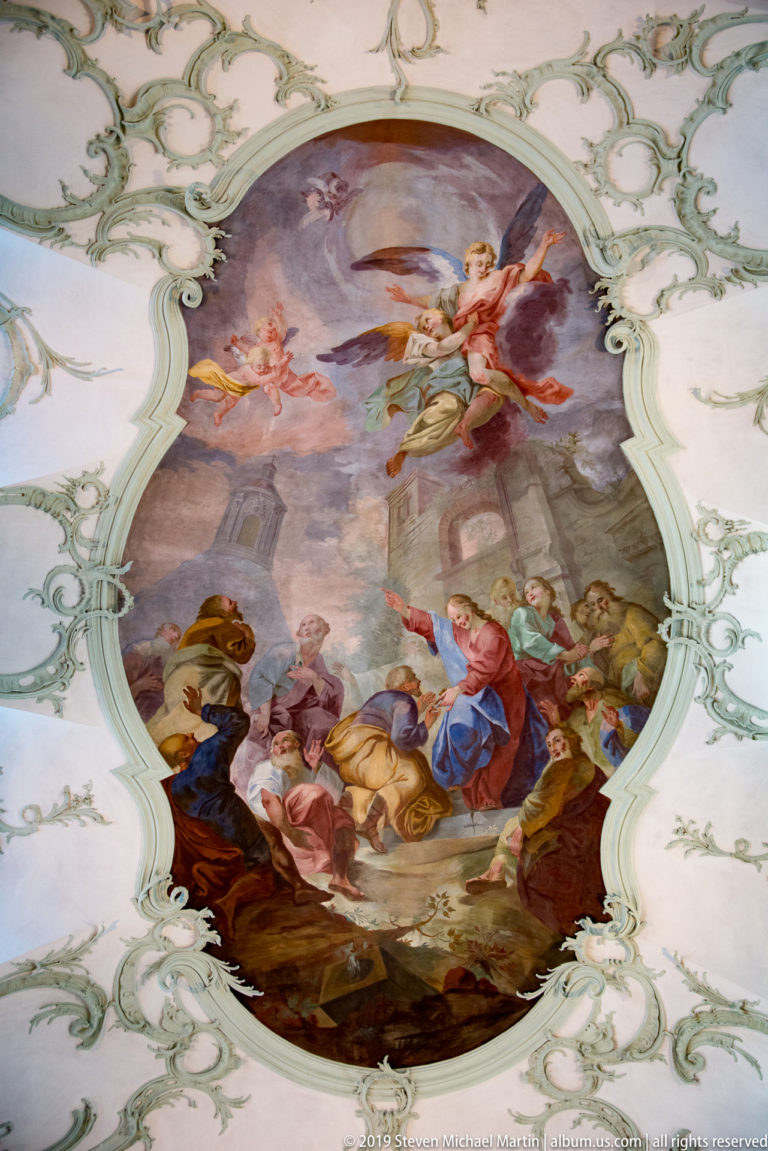 Oval ceiling fresco with a multi-figure religious scene framed by pale scrolling Rococo stucco.