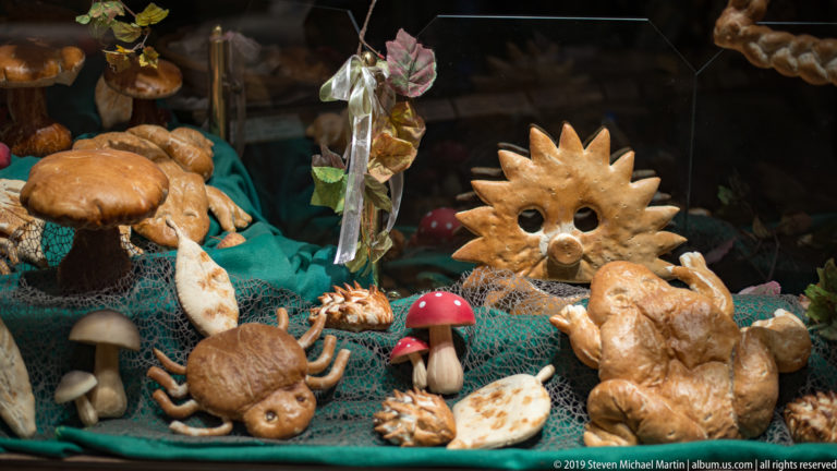 Whimsical bread display with a sun face, mushrooms, animal shapes, and sculpted pastries arranged over green netting.