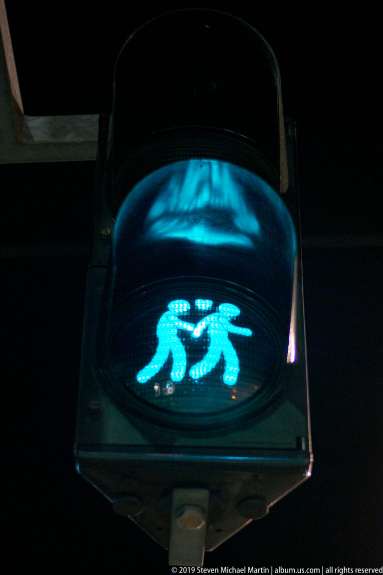 Dark pedestrian signal displaying two turquoise walking figures made from a grid of small lights.