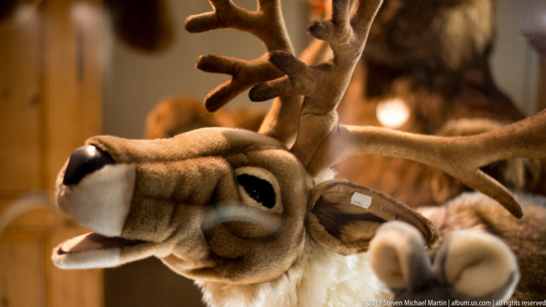 Close view of a plush reindeer with large branched antlers, black nose, and open mouth in a toy display.