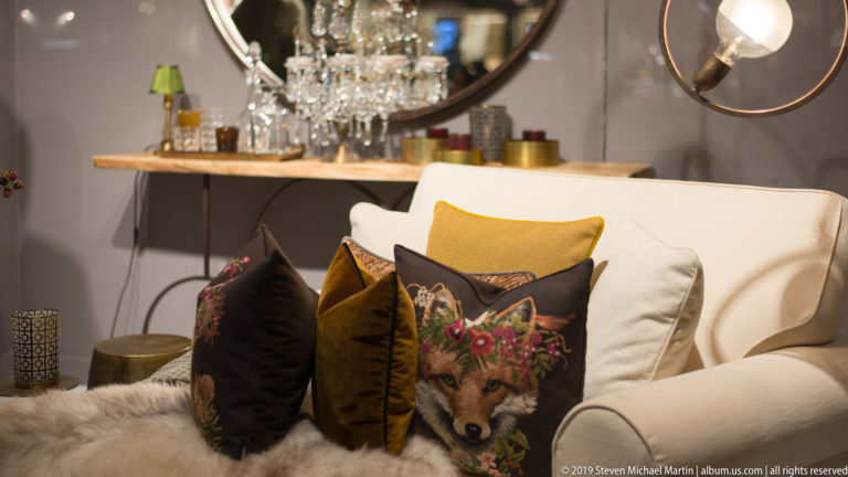 White boutique seating with velvet cushions, a fox-print pillow, fur-textured throw, and hanging lights.