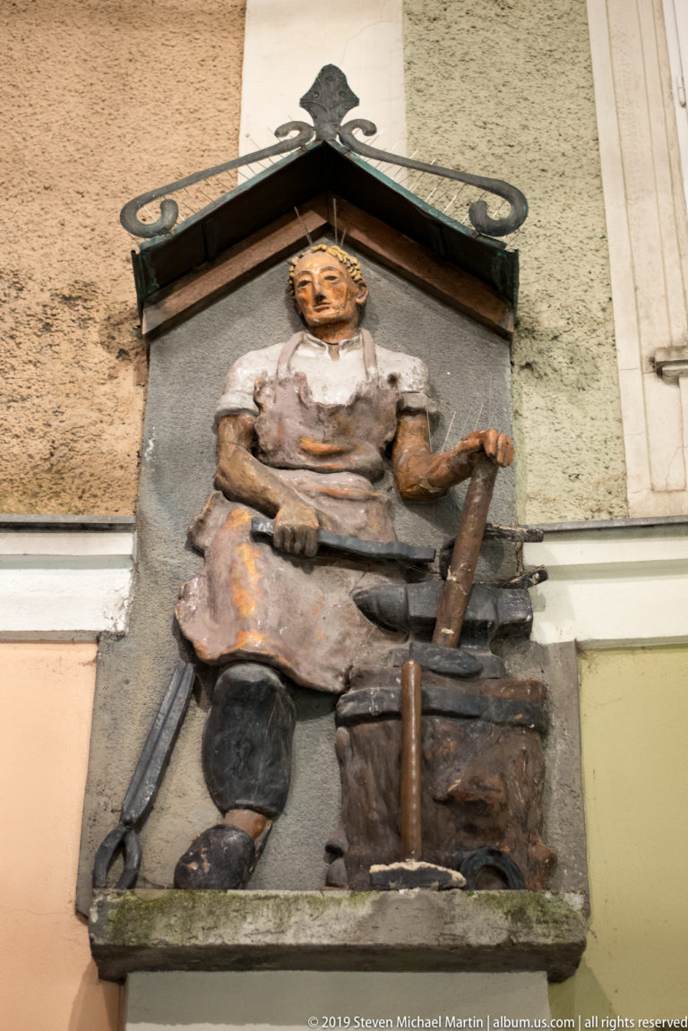 Painted wall relief of a seated craftsman surrounded by tools and working at a bench or block.
