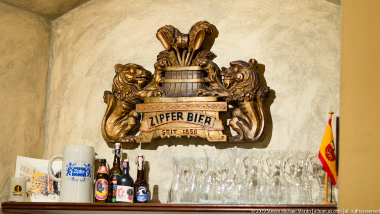Ornate Zipfer Bier seit 1858 wall emblem with heraldic lions above glasses, beer bottles, and a small Salzburg flag.