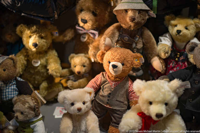Crowded display of teddy bears in different sizes and costumes under warm shop lighting.