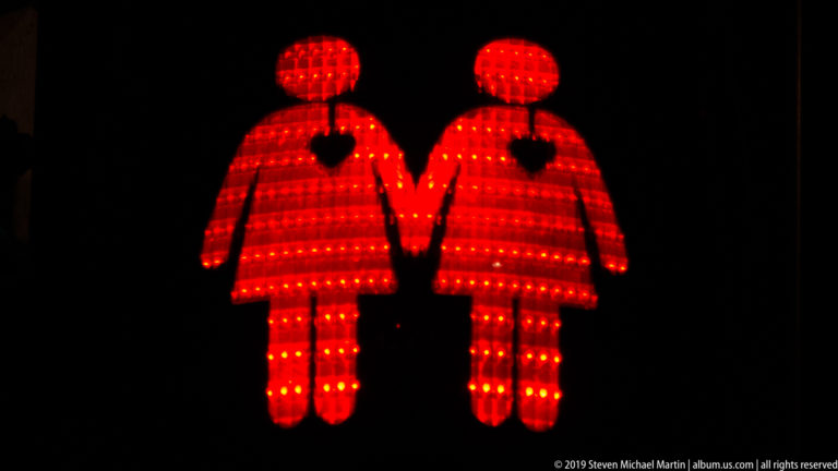 Two red illuminated human figures holding hands against a black background.