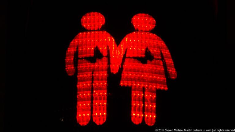 Two red illuminated figures holding hands, each with a dark heart shape cut out of the chest.