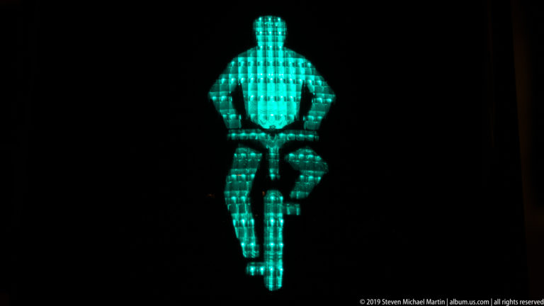 Turquoise illuminated human figure with bent legs against a black background.