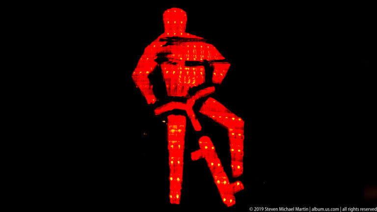 Red illuminated adult figure leaning toward a smaller child figure against a black background.