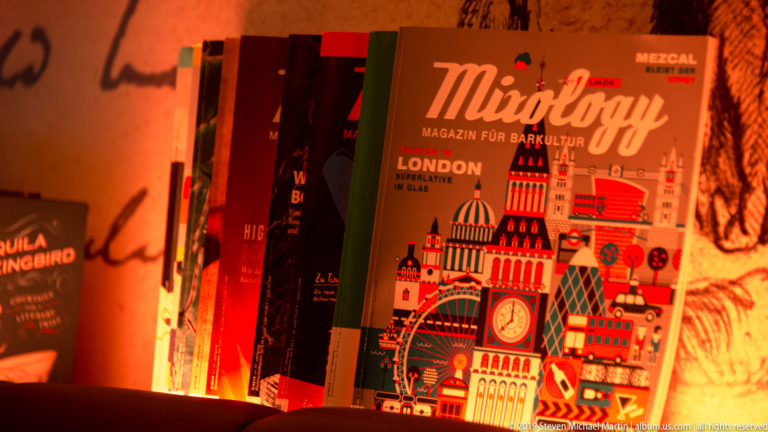 Warm orange-lit display of Mixology magazines, with a London-themed illustrated cover facing forward.