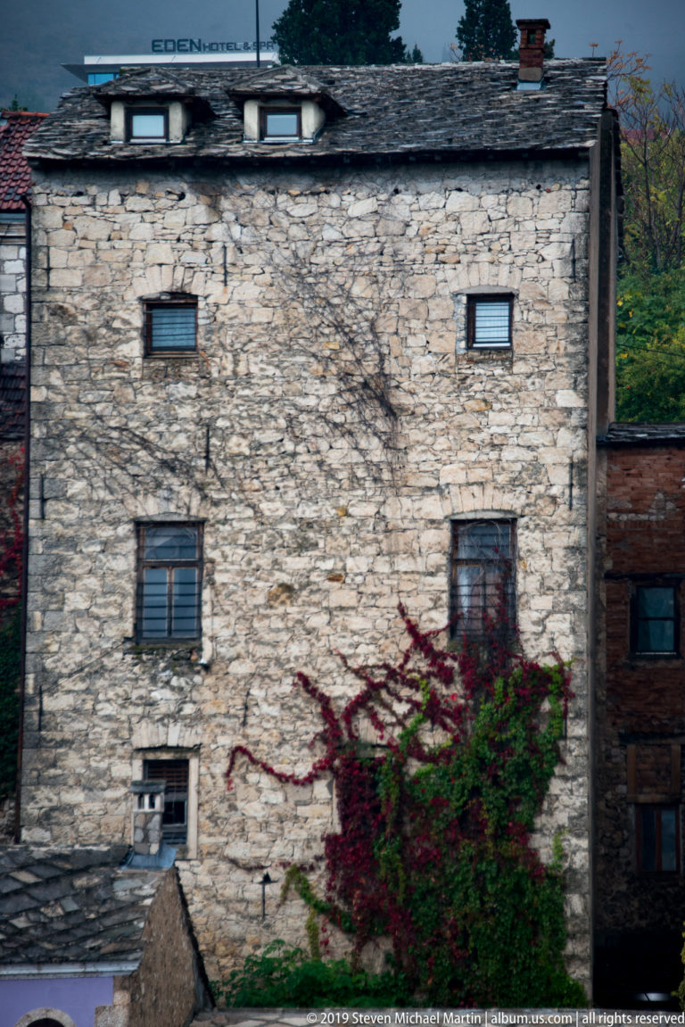 Weathered rubble-stone house with small windows, stone-slab roof, and red autumn vine.