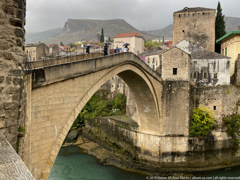 Close view of Stari Most stone arch and Tara Tower with pedestrians crossing the bridge.