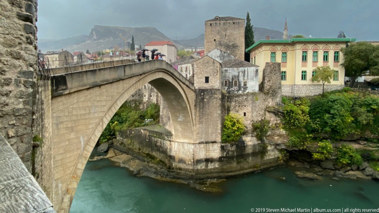 Stari Most arch meeting a massive square stone bridge tower beside the Neretva in Mostar.