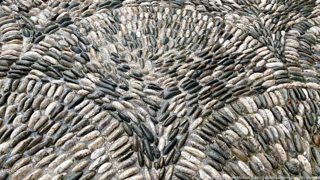 Close view of smooth gray river stones arranged in radiating fan patterns as pavement.