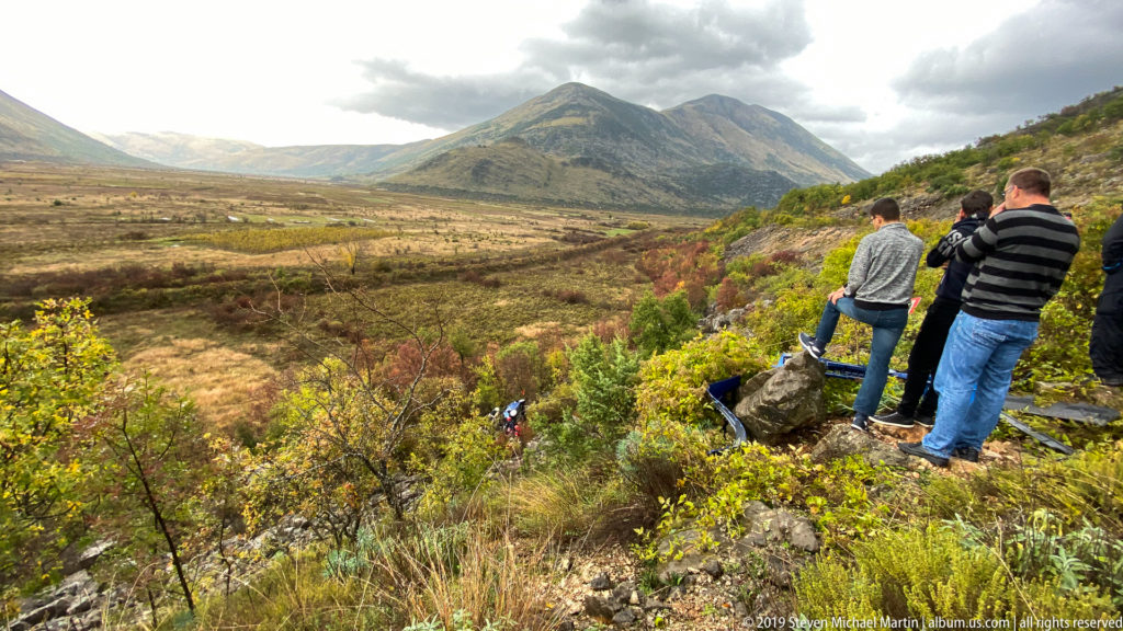 Three people on a rocky overlook above an autumn valley and rugged mountains near Mostar.