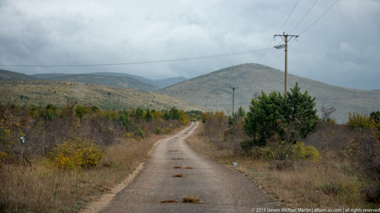 Narrow paved road and utility poles cross scrubby karst hills beneath a cloudy sky.