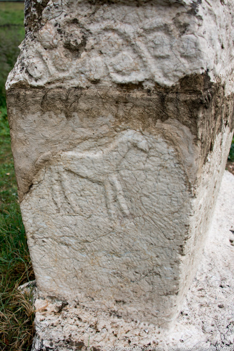 Weathered limestone stećak with a shallow carved human figure visible on its side panel.