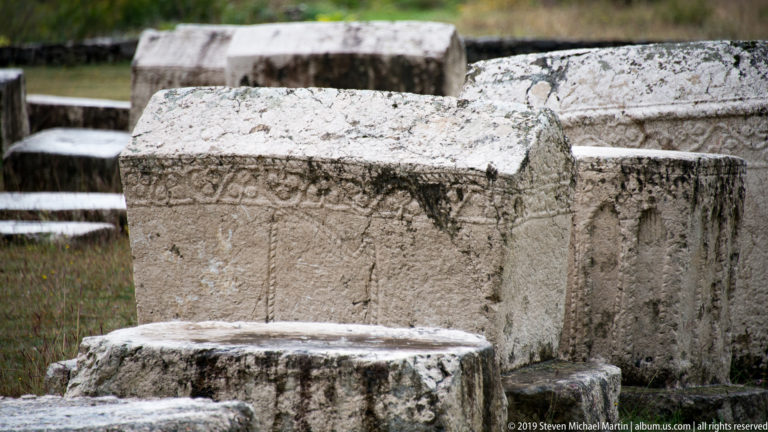 Large gabled stećak with a carved border and faint central relief surrounded by neighboring stone tombs.