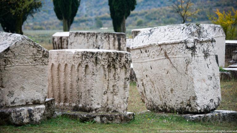 Three carved stećci with fluting, gabled tops, and ornamental borders stand together in the cemetery.