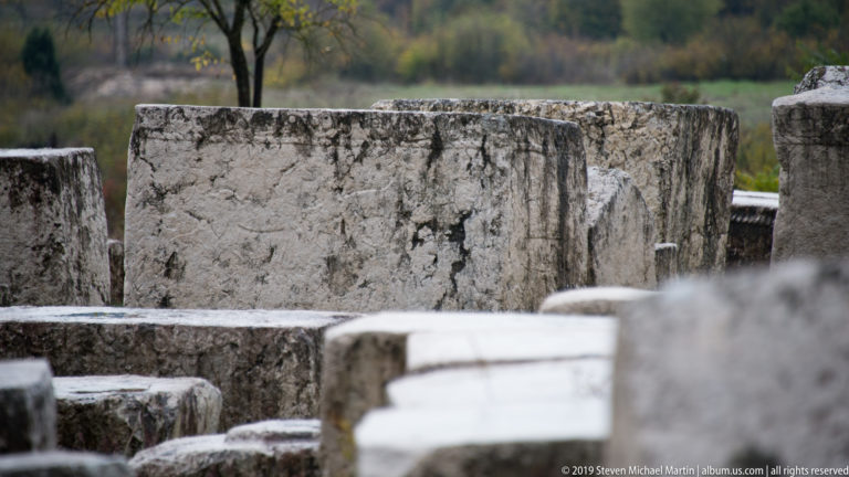 Large weathered rectangular stećci overlap closely, with a central pale stone block in sharp focus.