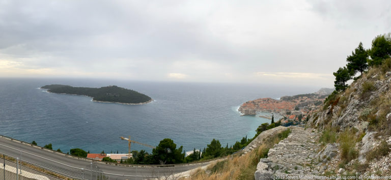 Lokrum island and Dubrovnik coast seen beyond a mountain road and pale rocky slope.
