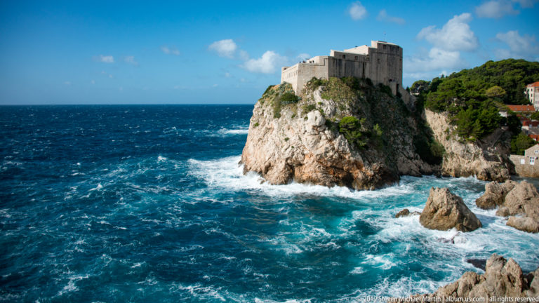 Fort Lovrijenac crowns a rocky cliff above white surf, with open deep-blue Adriatic water filling the left side.