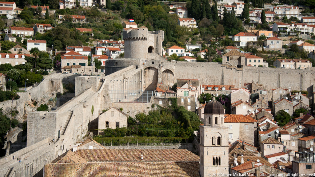Round stone tower, high curtain walls, and an arched approach rise above red-tiled houses on Dubrovnik’s western side.