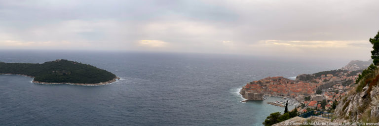 Lokrum island offshore with Dubrovnik’s Old Town at right, seen from a high rocky hillside.