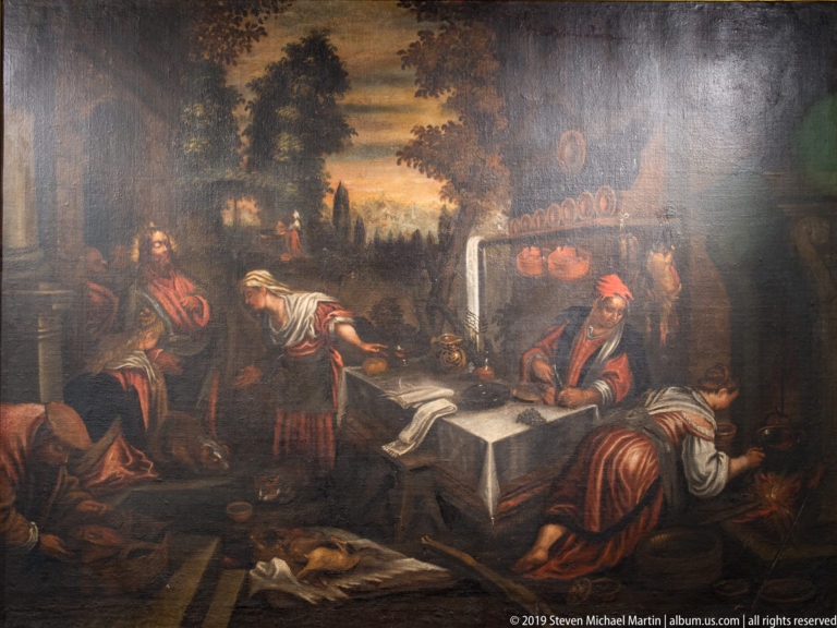 Dark narrative painting with several robed figures gathered around a table in an interior, including a seated man in red.