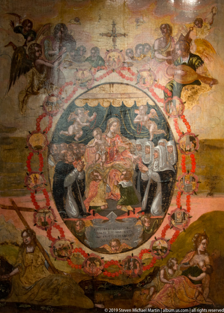 Aged circular ceiling painting with central heraldic or allegorical scene, ornamental border, and many surrounding figures.