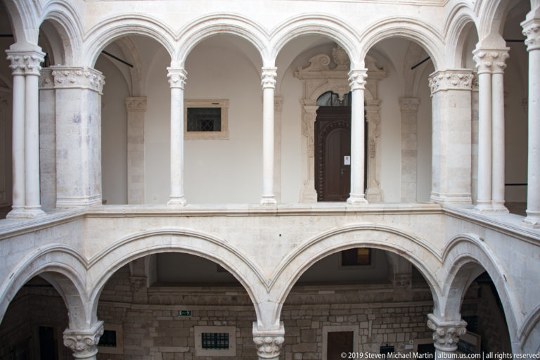 Two-story pale stone arcade in the Rector’s Palace courtyard with broad lower arches and slender-column upper gallery.