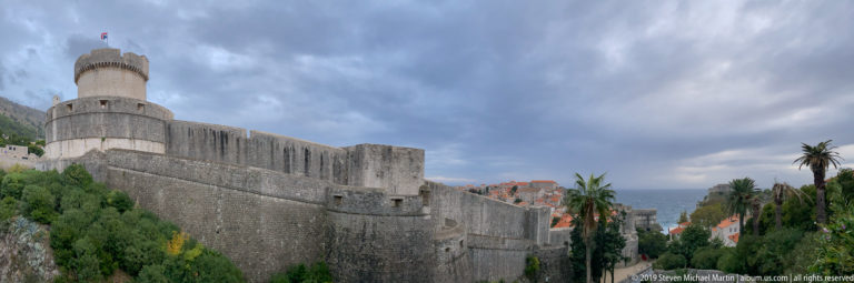 Massive rounded stone defensive tower connected to high Dubrovnik walls beneath dark clouds.