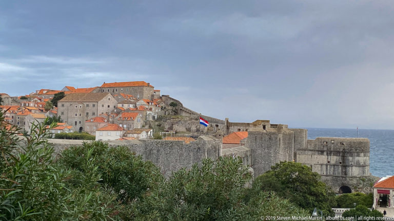 Elevated view of Dubrovnik’s red-roofed Old Town enclosed by stone walls beside the Adriatic.
