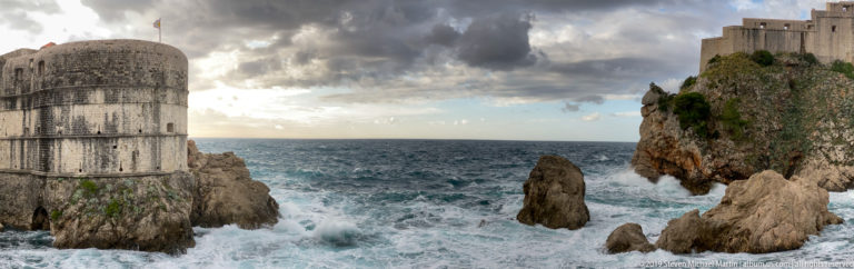 Massive Dubrovnik stone fortifications above rough sea, with a rock stack between the walls.