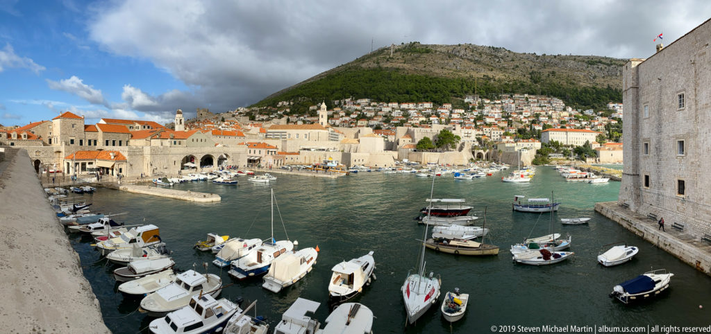 Boats moored in Dubrovnik Old Port below stone walls, red roofs and hillside houses.