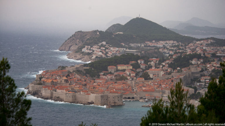 High view of Dubrovnik’s walled Old Town with a densely settled coastal peninsula beyond.
