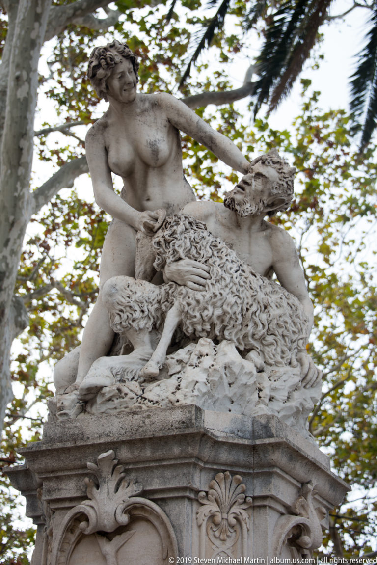 Large classical-style stone sculpture with intertwined human figures and animal atop ornate pedestal.