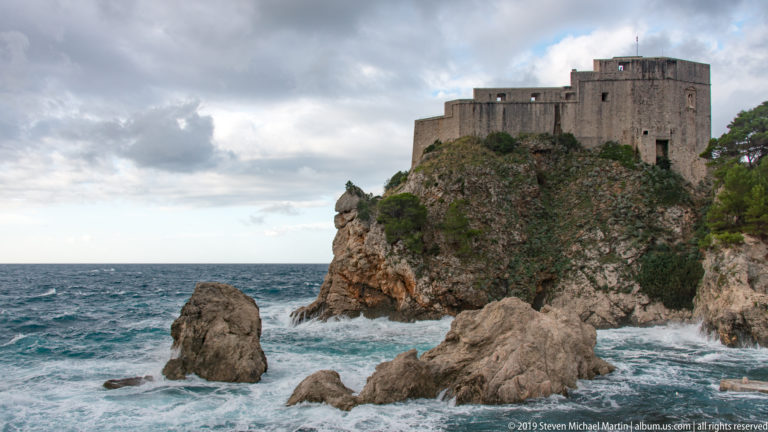 Fort Lovrijenac on a rocky promontory above rough Adriatic water and sea stacks.